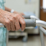 Close-up of an elderly nursing home resident’s hand gripping a walker handle for support